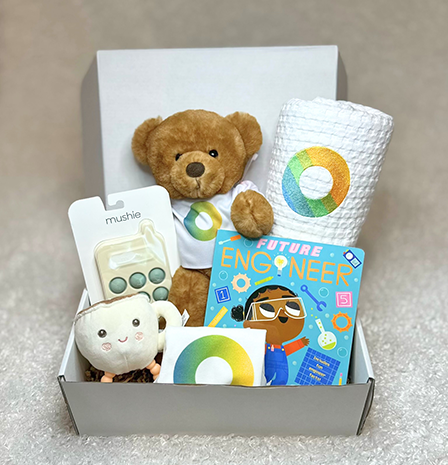 Gift box with a brown teddy, a plush bear, a 'Future Engineer' book, a circular-logo cup, and small packaged toys arranged in tissue paper.